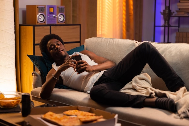 怠惰な男はソファに横たわってリラックスしたアフロ男筋肉はメッセージを送信しますソーシャルメディアはビデオを見る