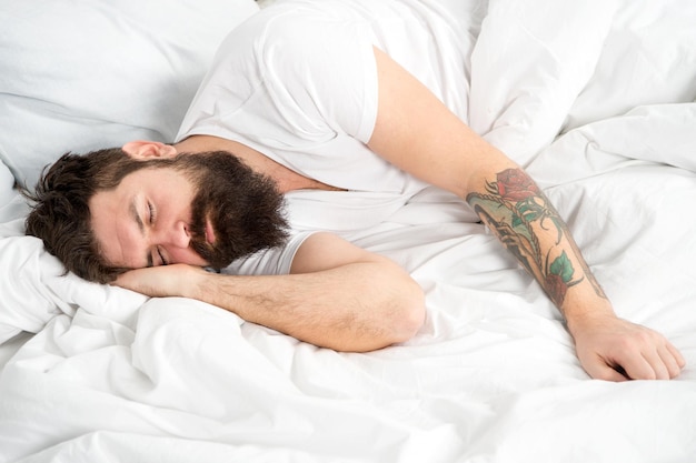 Lazy morning Man bearded hipster sleepy in bed Early morning hours Insomnia and sleep problems Relax and sleep concept Man bearded guy sleep on white sheets Healthy sleep and wellbeing