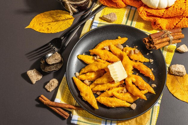 Lazy pumpkin dumplings, gnocchi with butter and brown sugar. Warm autumn dish, sweet healthy food. Black stone concrete background, trendy hard light, dark shadow, top view