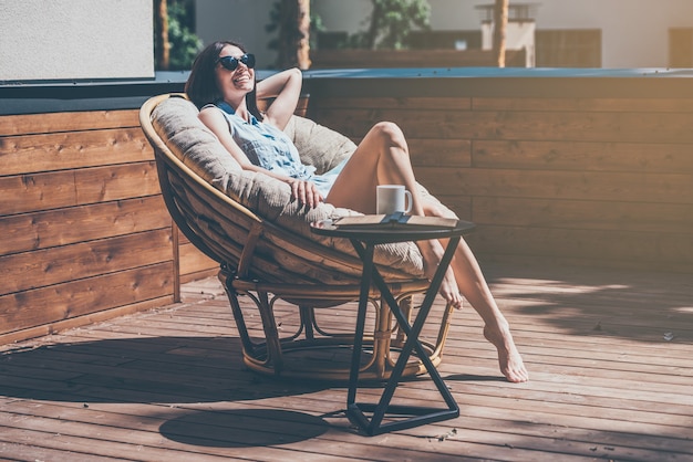 Lazy time in comfortable chair. Beautiful young woman relaxing in a big comfortable chair on her outdoor house terrace