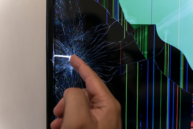 LCD 모니터 화면이 깨졌습니다. 남자의 손이 균열을 만집니다.