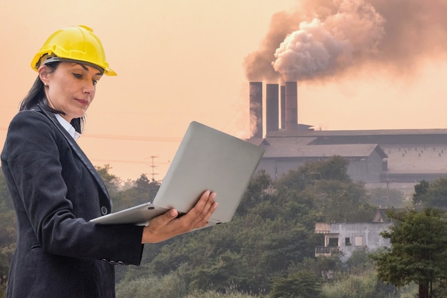 Ingegnere donna leader che tiene in mano un laptop che controlla il fumo ardente sul camino in background in fabbrica