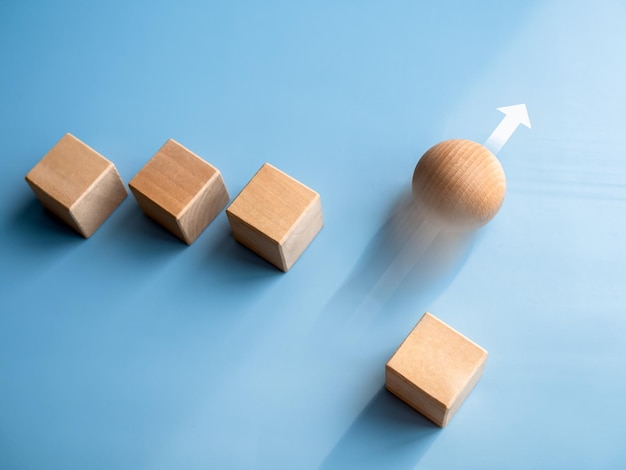 リーダーシップのビジネスの成功独自の違いの課題とモチベーションのコンセプト木製の球体が最速で回転し、上昇矢印で先頭に立ち、青い背景に木製の立方体ブロックが続きます