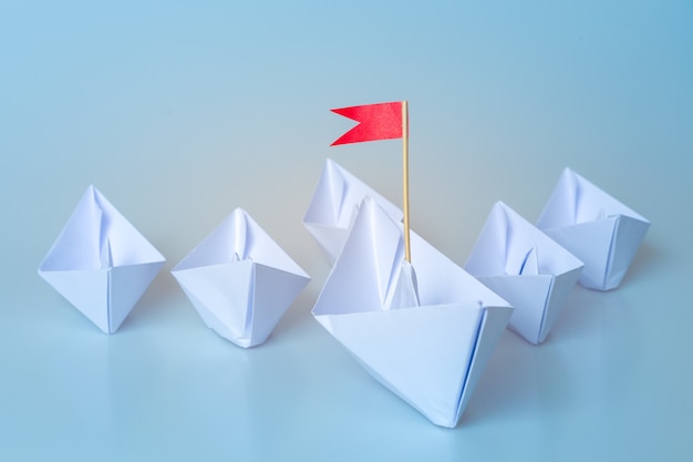 Leadership concept using  paper ship with red flag on blue background