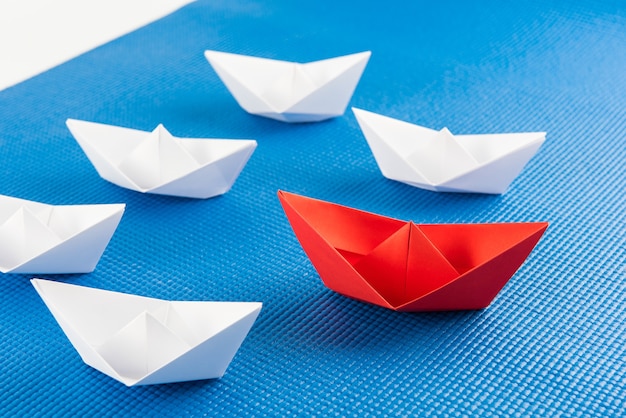 Концепция лидерства с красным бумажным кораблем, ведущим среди белого и синего фона