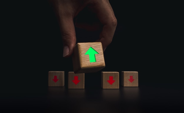 Leadership, development, and think different concepts. hand\
putting the wooden cube block with green, up arrow in front of the\
red down arrow blocks on dark background.