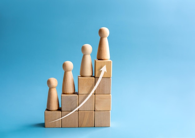 Leadership with business success concept Modern rising up arrow and wooden figures standing on a growth graph chart steps arranged by wood cube blocks isolated on blue background with copy space