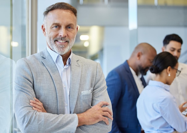 Leading a thriving empire Portrait of a mature businessman standing in an office with his colleagues in the background