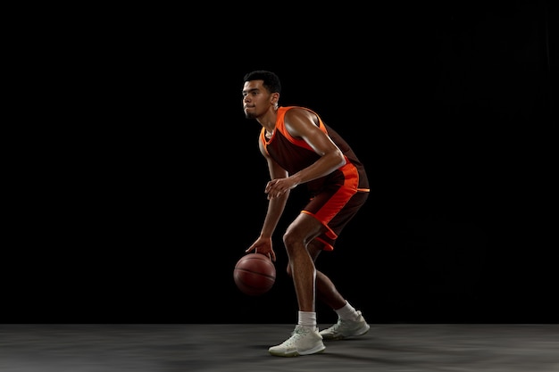 Leading. Young purposeful african-amrican basketball player training, practicing in action, motion isolated on black background. Concept of sport, movement, energy and dynamic, healthy lifestyle.