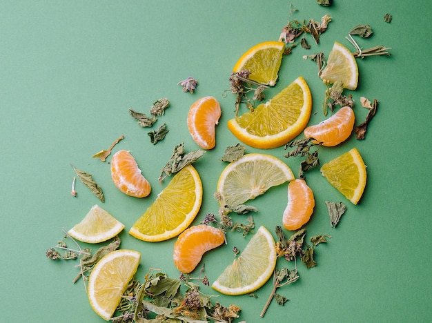 Leaf tea with orange and tangerine slices on green background