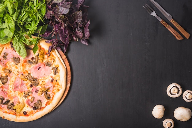 Leafy vegetable; mushroom and pizza with cutlery on dark backdrop