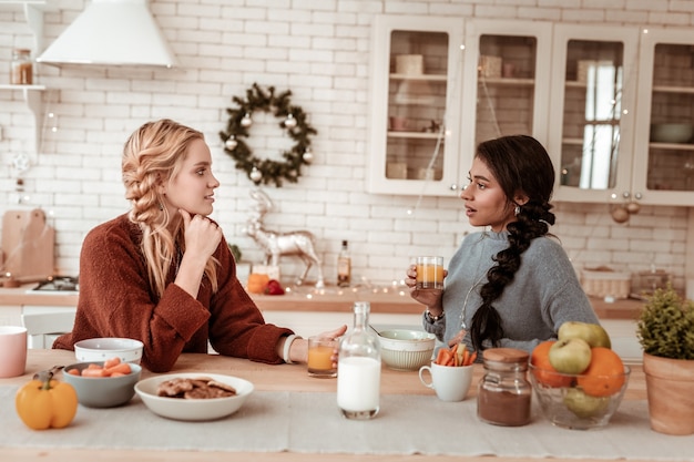 Leaning on table. Thoughtful blonde lady leaning on hand and listening to friend while she telling story