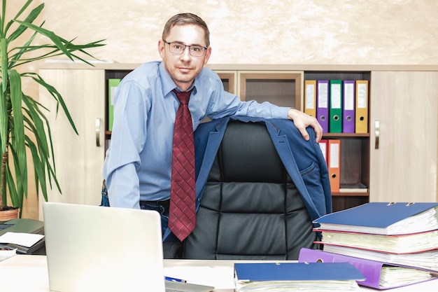 Leans with his hand on the back of the bracket on which the jacket hangs Successful office worker