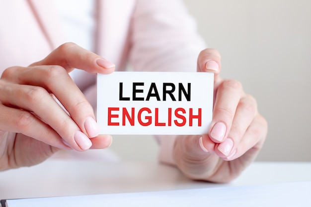 Learn english is written on a white business card in a woman's hands. Pink background. Business and advertising concept