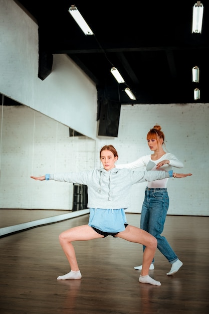 Learn to squat. Dark-haired pretty teenager wearing black shorts doing squatting at the dance lesson