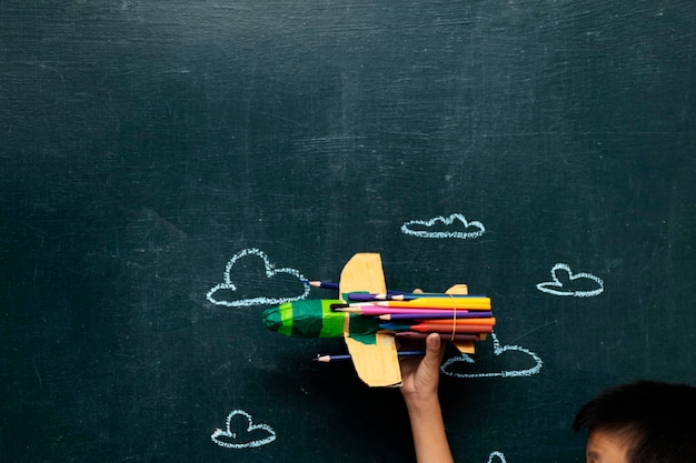 Learning concept with Paper rocket made from pencils over chalkboard background Children are holding it to float