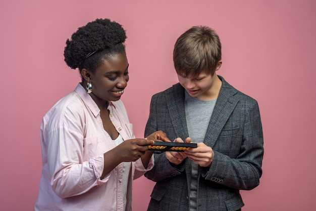 Learning, count. Dark-skinned smiling woman teaching caucasian guy with down syndrome counting on abacus standing on light background