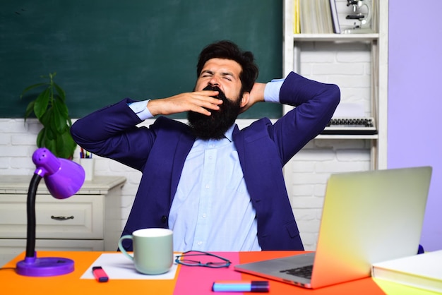 Photo learning and education yawning male university student indoors bearded teacher near chalkboard in