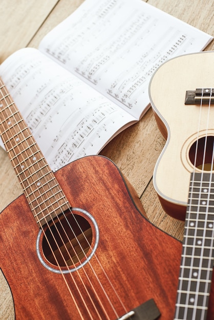 Learning how to play guitar. Vertical close up photo of acoustic and ukulele guitars lying on the wooden floor with music notes. Top view. Music equipment. Music shop. Musical instruments