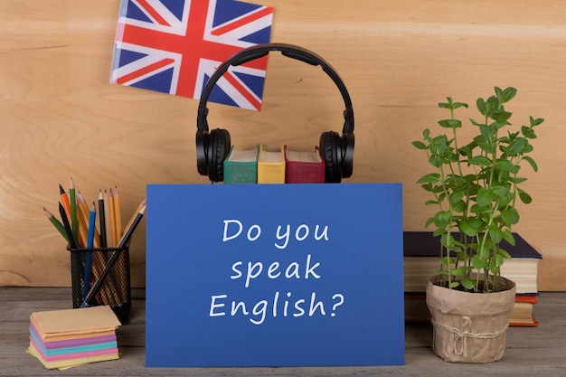 learning languages concept - blue paper with text "do you speak english?", flag of the great britain, headphones, books and chancellery on the table