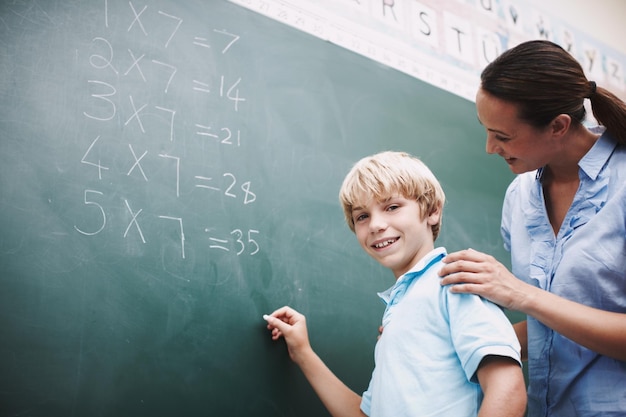 Learning teacher or student portrait at chalkboard in classroom for solving math problem or answer equation Lesson boy and writing multiplication solution at school with education support and help