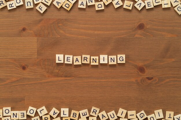 写真 「学習」という言葉のテキストは、木製のオフィスの机に分離された木製の文字で書いた。