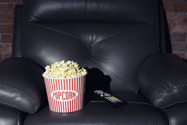 Leather armchair with popcorn and remote control in home cinema