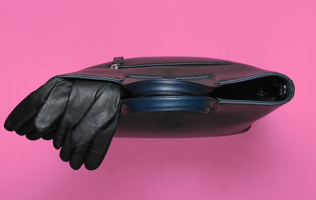 Фото Кожаная сумка и перчатки на розовом бумажном фоне. минималистичный модный натюрморт. плоская планировка. вид сверху