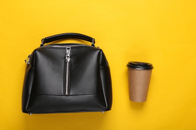 Leather bag and coffee cup on yellow background Top view