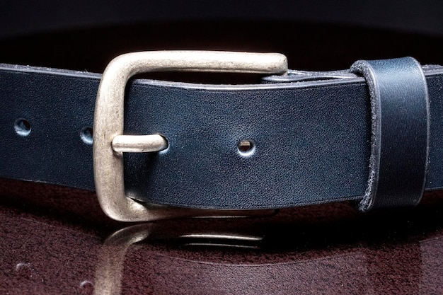 Leather belt with a metal buckle close-up on a dark background.