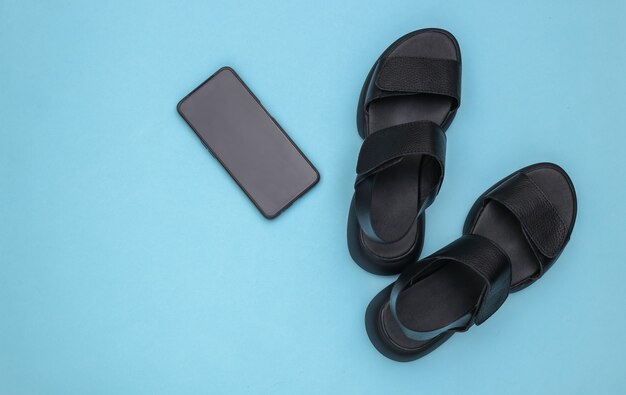 Leather black women's sandals and smartphone on blue background. Top view. Flat lay