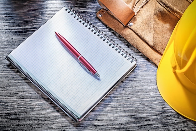 Leather construction belt building helmet notepad pen on wooden board.