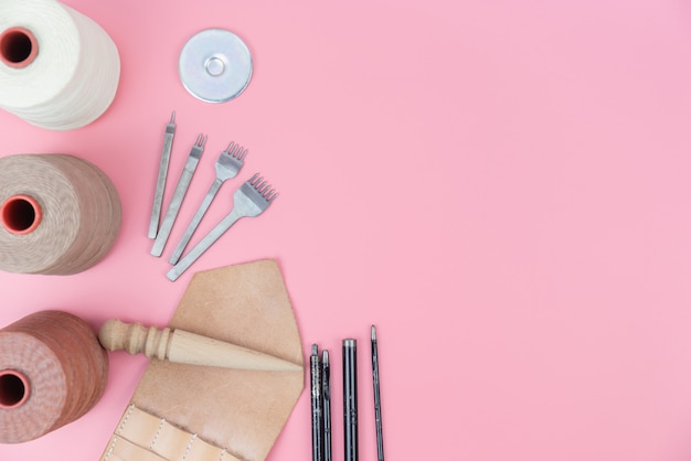 Foto gruppo di strumenti artigianali in pelle con corda cerata e forma pugno su sfondo rosa pastello