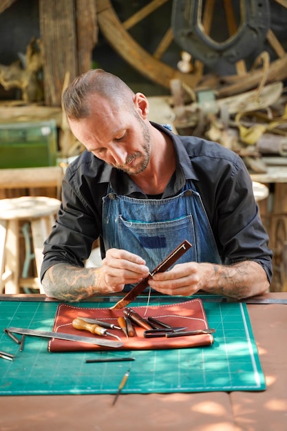 A leather craftsman is working hard to sew a leather product for a customer