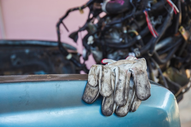 Leather gloves on car body chassis frame with blurred car engine background