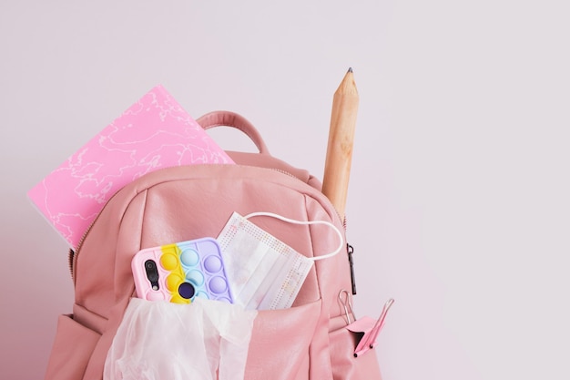 Photo leather pink backpack with a head, a smartphone with a pop it case, pencil and a notebook, back to school concept