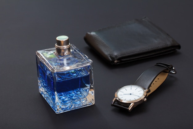 Leather purse, watch with a black leather strap and cologne for men on the black background. Accessories for men. Selective focus on bottle of perfume.