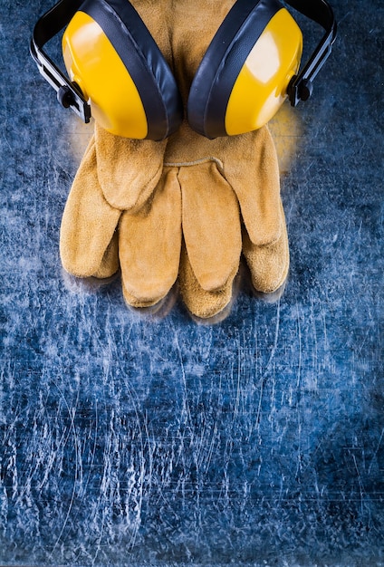 Leather safety gloves and noise insulation ear muffs on scratched metallic background copy space image construction concept