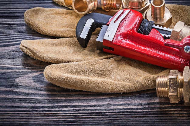 Leather safety gloves pipe wrench brass plumbing connectors on wooden board.