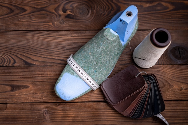 Leather samples for shoes and plastic shoe last on dark wooden table