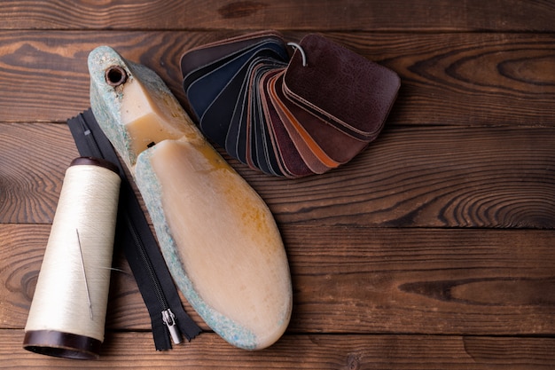 Leather samples for shoes and plastic shoe last on dark wooden table