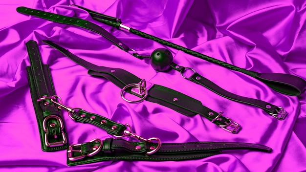 Leather straps handcuffs collar gag ball and whip on a satin sheet