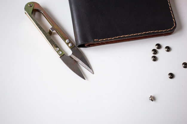 Photo leather wallet in black lies next to rivets and metal tools for leatherworking, leather product