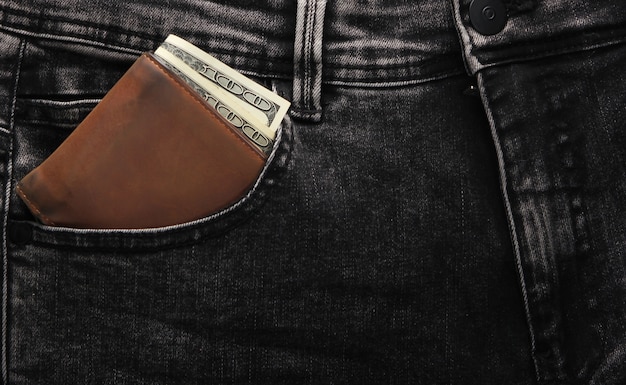 グレーのジーンズのフロントポケットに百ドル札が入った革の財布