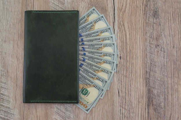 Leather wallet with US dollars on a wooden table.