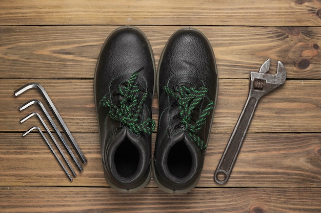 Leather work boots and set of wrench on wooden background. Top view