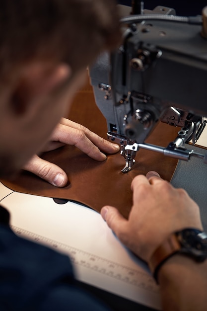 Leatherworker workflow. A tanner or skinner sews leather on a special sewing machine. A worker sews on a sewing machine, a shot from behind the master.