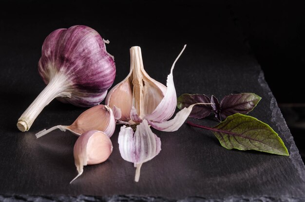 Photo leaves of basil and garlic on black stone table on black background