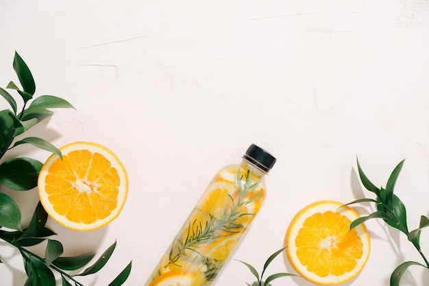 Leaves and bottle tropical water on white background Detox fruit infused water citrus fruits and rosemary leaves Top view flat lay copy space