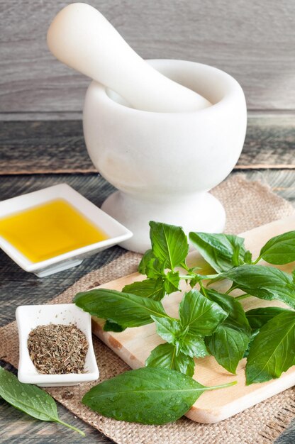 The leaves of fresh basil on a chopping board olive oil dried basil spices and mortar on a wooden table rustic style